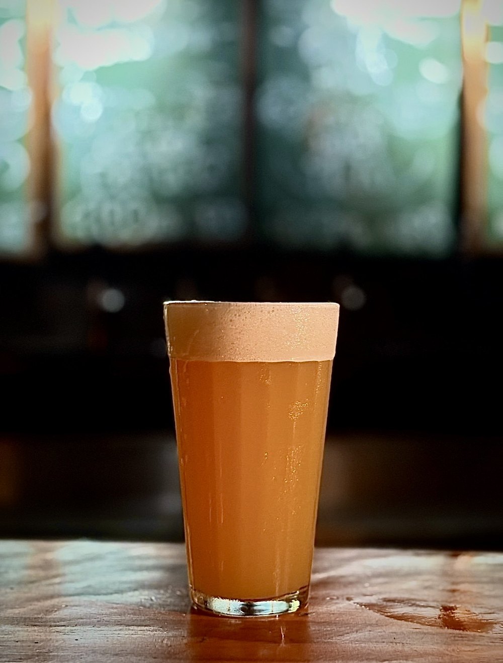 The IPA glass on the wooden table, the window behind.