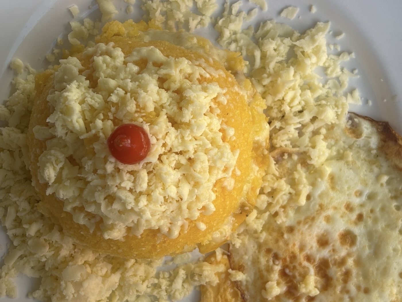 Cuscuz covered in cheese with a tomato on top, next to a fried egg.