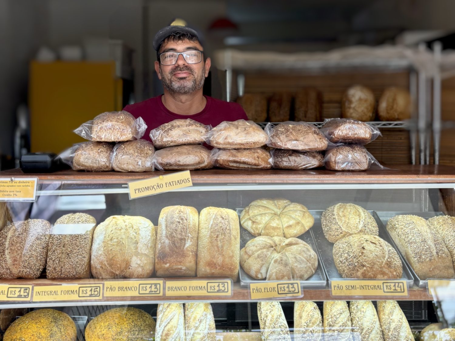 Miquel behind the counter at Pão Saudável Itacaré, bread on display.