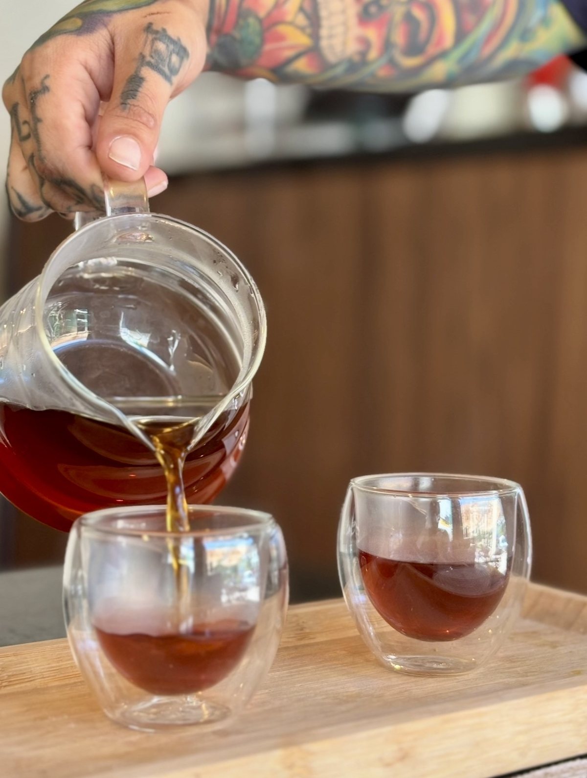 Coffee being poured from the glass jug into two cups, at the counter.