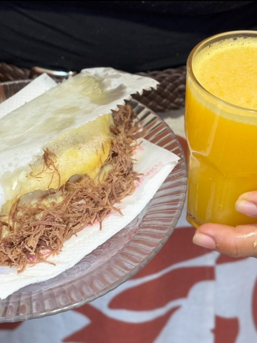 Tapioca de carne de sol no prato, ao lado de um copo de suco de laranja.