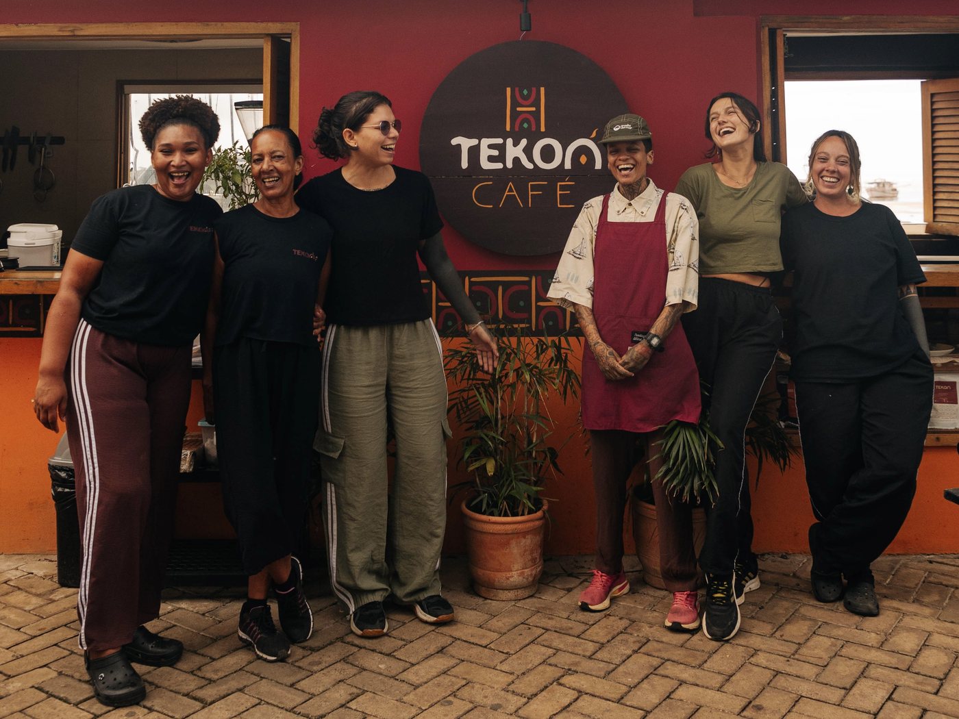 The TEKOÁ Café team in front of the red façade, under the sign.