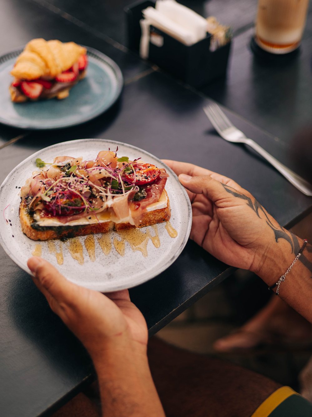 Hands serving the toast with parma ham, brie and honey on a ceramic plate.